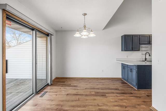 unfurnished dining area with baseboards, visible vents, wood finished floors, a chandelier, and a sink