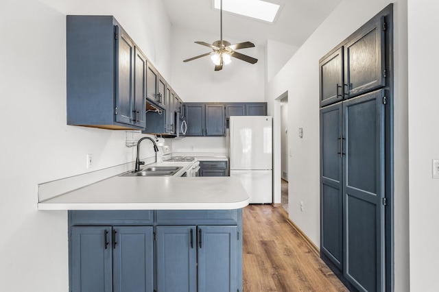 kitchen with a peninsula, a sink, light countertops, freestanding refrigerator, and stainless steel microwave