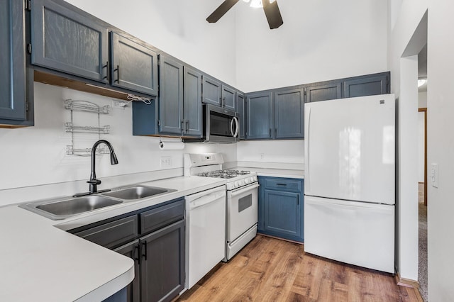 kitchen featuring white appliances, a high ceiling, a sink, light wood-style floors, and light countertops