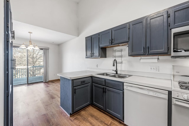 kitchen featuring a peninsula, white appliances, wood finished floors, a sink, and light countertops