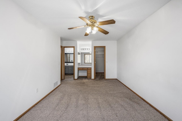 unfurnished bedroom with connected bathroom, light colored carpet, visible vents, baseboards, and a walk in closet