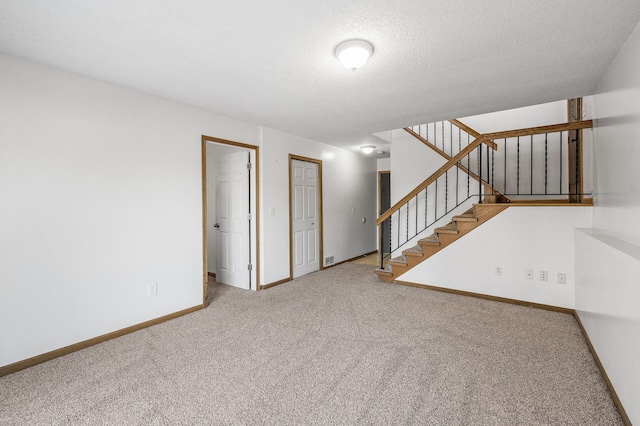 interior space featuring a textured ceiling, carpet floors, visible vents, baseboards, and stairway