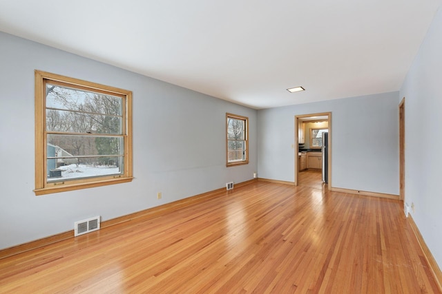 empty room featuring light wood-type flooring, visible vents, and baseboards