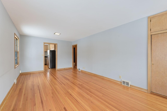 empty room with light wood finished floors, baseboards, and visible vents