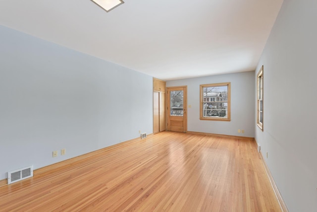 empty room featuring light wood-style floors, visible vents, and baseboards