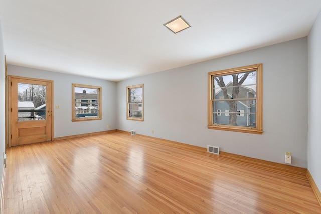 spare room with light wood-type flooring, visible vents, and baseboards