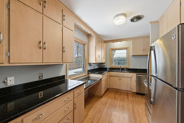 kitchen featuring stainless steel appliances, a sink, light wood-style floors, ornamental molding, and dark stone counters