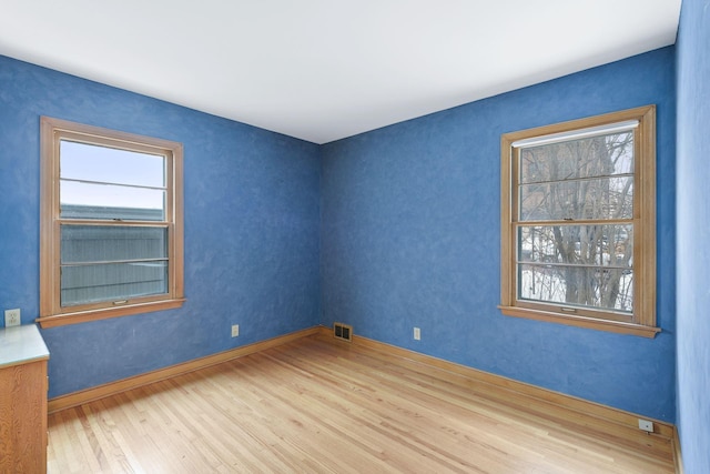 unfurnished room featuring baseboards, visible vents, and wood finished floors