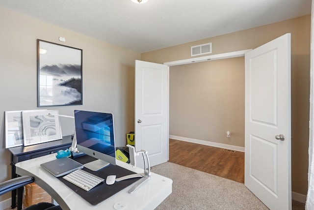 carpeted office space featuring visible vents, a textured ceiling, and baseboards