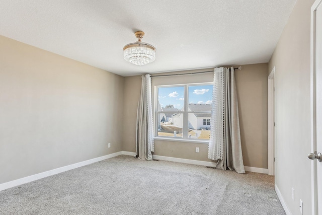 spare room featuring a notable chandelier, carpet flooring, baseboards, and a textured ceiling