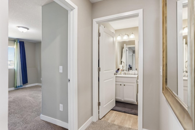 corridor featuring a textured ceiling, a sink, baseboards, and light carpet