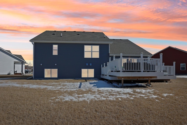 snow covered back of property with a wooden deck and roof with shingles