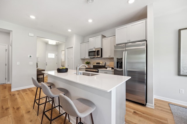 kitchen with light wood finished floors, stainless steel appliances, backsplash, a sink, and a kitchen breakfast bar