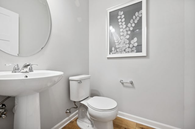 bathroom with a sink, toilet, baseboards, and wood finished floors