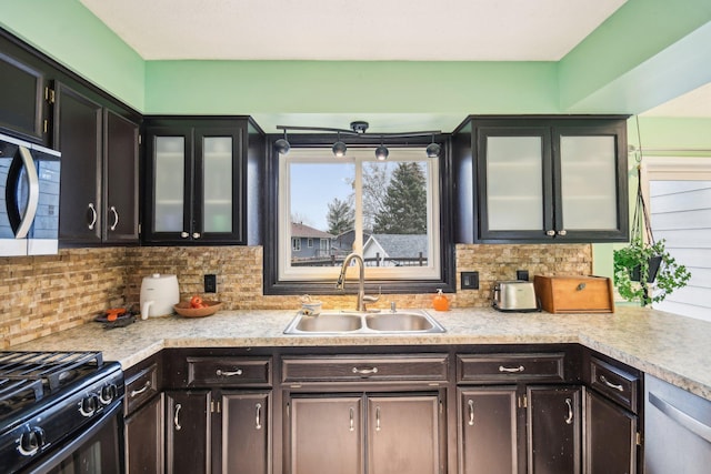 kitchen with stainless steel appliances, tasteful backsplash, light countertops, glass insert cabinets, and a sink