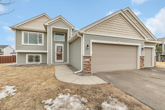 view of front of house featuring stone siding, driveway, an attached garage, and fence