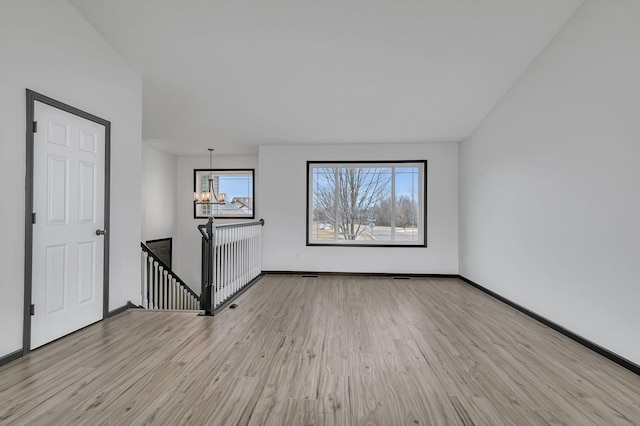 empty room featuring a healthy amount of sunlight, an inviting chandelier, light wood-style flooring, and baseboards