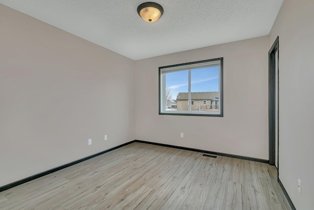 empty room featuring a textured ceiling, light wood finished floors, visible vents, and baseboards