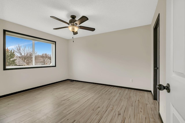 spare room featuring light wood finished floors, a ceiling fan, and baseboards