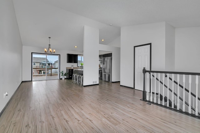 unfurnished living room featuring a notable chandelier, recessed lighting, high vaulted ceiling, light wood-type flooring, and baseboards