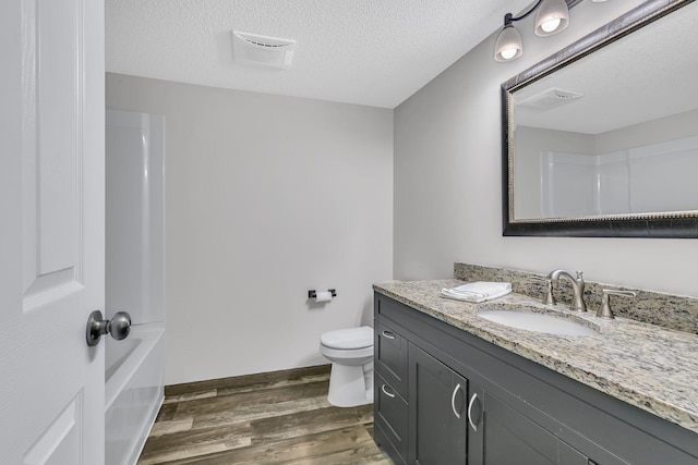 full bathroom featuring toilet, a textured ceiling, vanity, wood finished floors, and baseboards