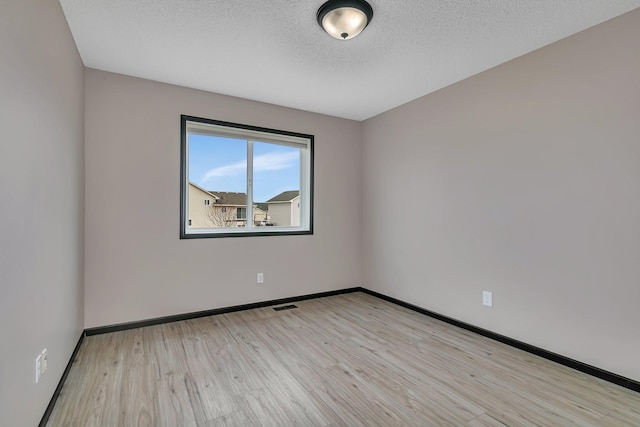 spare room featuring light wood finished floors, visible vents, baseboards, and a textured ceiling