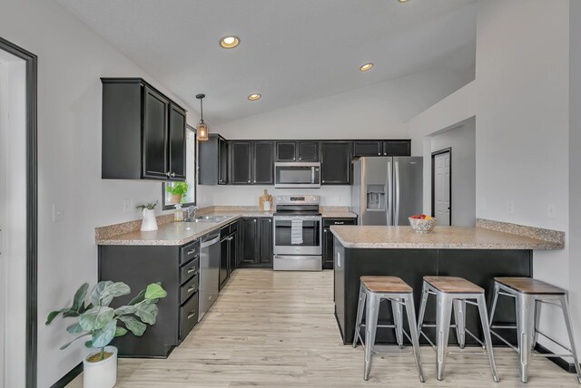 kitchen featuring lofted ceiling, a breakfast bar area, a peninsula, a sink, and appliances with stainless steel finishes