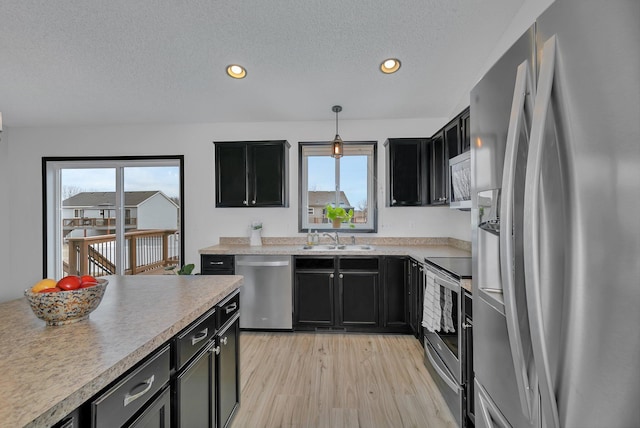 kitchen with a textured ceiling, light wood-style flooring, dark cabinets, light countertops, and appliances with stainless steel finishes