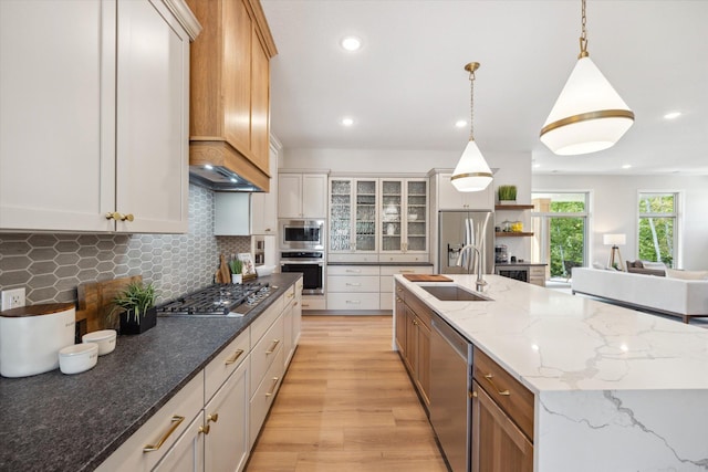 kitchen with a sink, decorative backsplash, an island with sink, stainless steel appliances, and light wood-style flooring