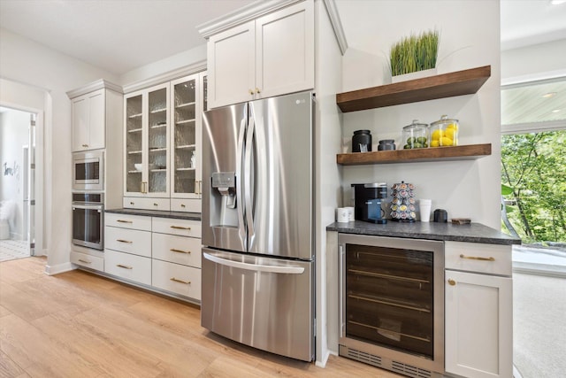 kitchen with dark countertops, beverage cooler, appliances with stainless steel finishes, and light wood-style flooring