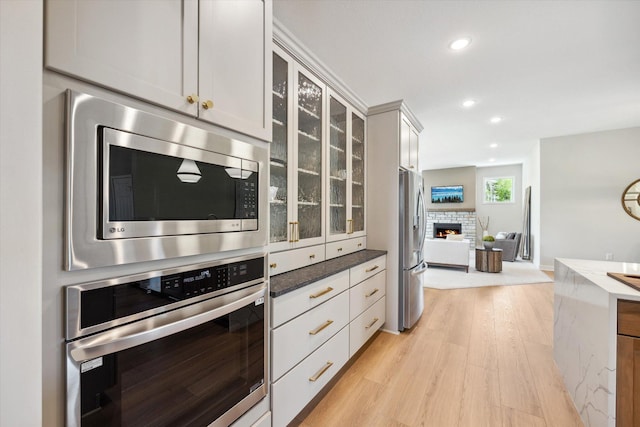 kitchen with light wood-type flooring, dark stone counters, glass insert cabinets, appliances with stainless steel finishes, and open floor plan
