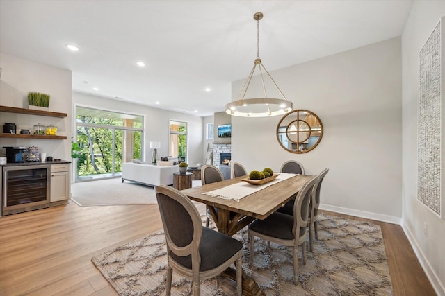 dining room with recessed lighting, beverage cooler, light wood-type flooring, baseboards, and a fireplace