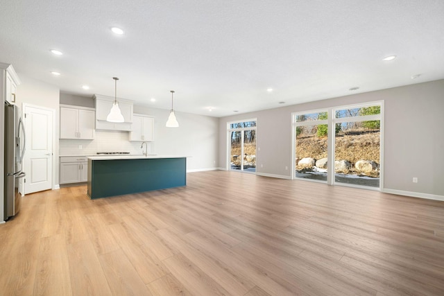 kitchen with decorative backsplash, stainless steel fridge with ice dispenser, open floor plan, a kitchen island with sink, and light wood-type flooring