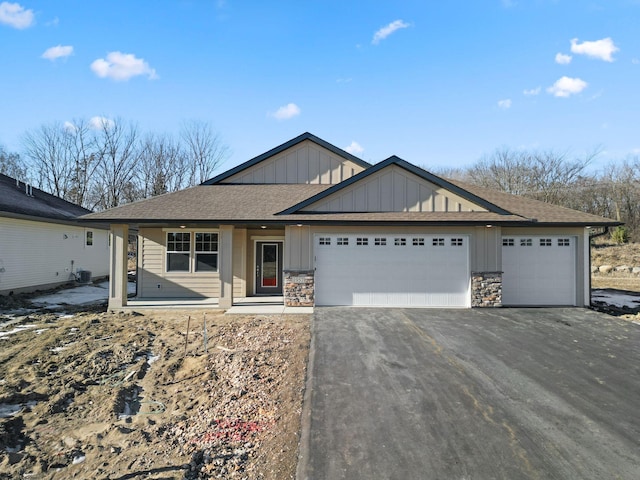 single story home featuring driveway, stone siding, roof with shingles, an attached garage, and board and batten siding