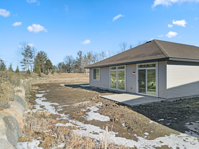 back of property with roof with shingles and a patio