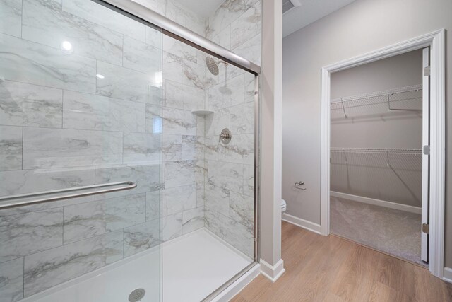 bathroom featuring a spacious closet, toilet, a stall shower, wood finished floors, and baseboards