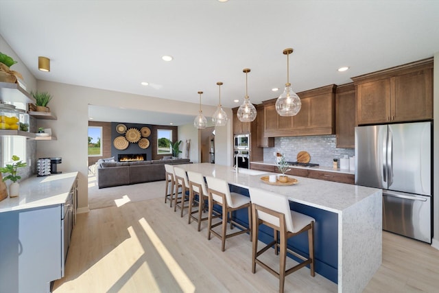 kitchen featuring light wood-style flooring, appliances with stainless steel finishes, a lit fireplace, a kitchen bar, and backsplash