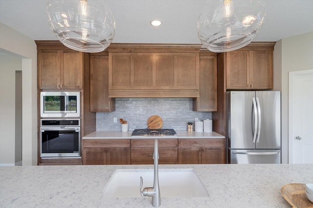 kitchen with a sink, range hood, appliances with stainless steel finishes, decorative backsplash, and brown cabinets