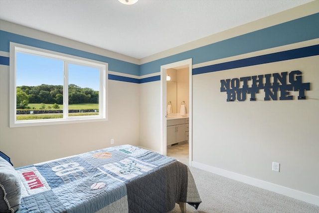 bedroom with baseboards, ensuite bathroom, and light colored carpet