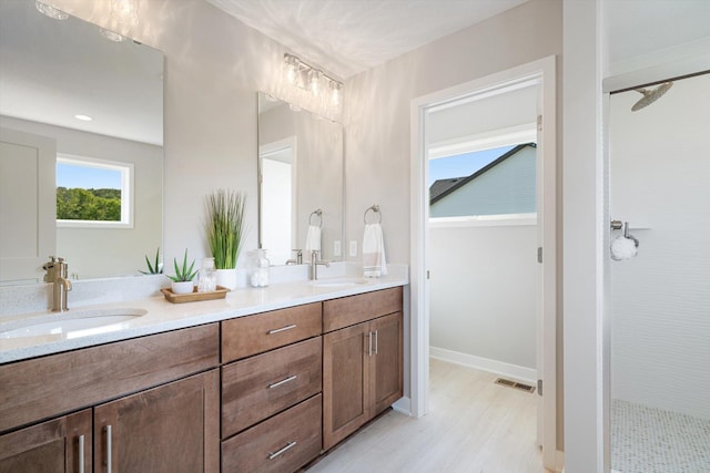 bathroom featuring a tile shower, double vanity, a sink, and visible vents