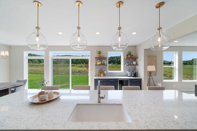 kitchen featuring light stone counters, open shelves, decorative backsplash, a sink, and beverage cooler