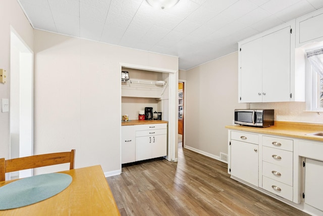kitchen with light wood-type flooring, light countertops, stainless steel microwave, and visible vents