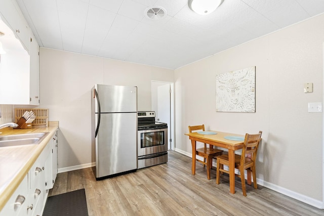 kitchen featuring a sink, stainless steel appliances, light wood finished floors, and visible vents