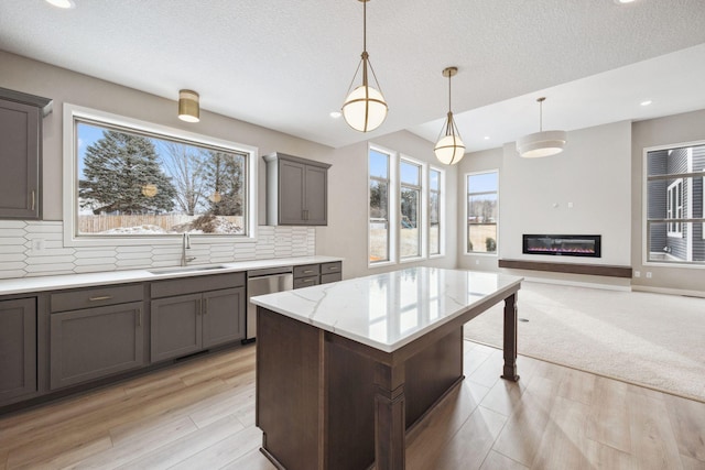 kitchen featuring gray cabinetry, a glass covered fireplace, open floor plan, a sink, and dishwasher