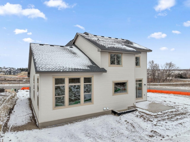 snow covered rear of property featuring a shingled roof