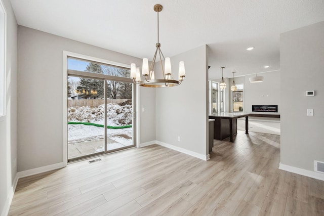 unfurnished dining area featuring light wood-style flooring, a glass covered fireplace, visible vents, and baseboards