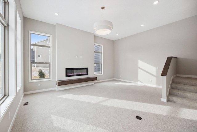 unfurnished living room with baseboards, a glass covered fireplace, stairs, carpet flooring, and recessed lighting