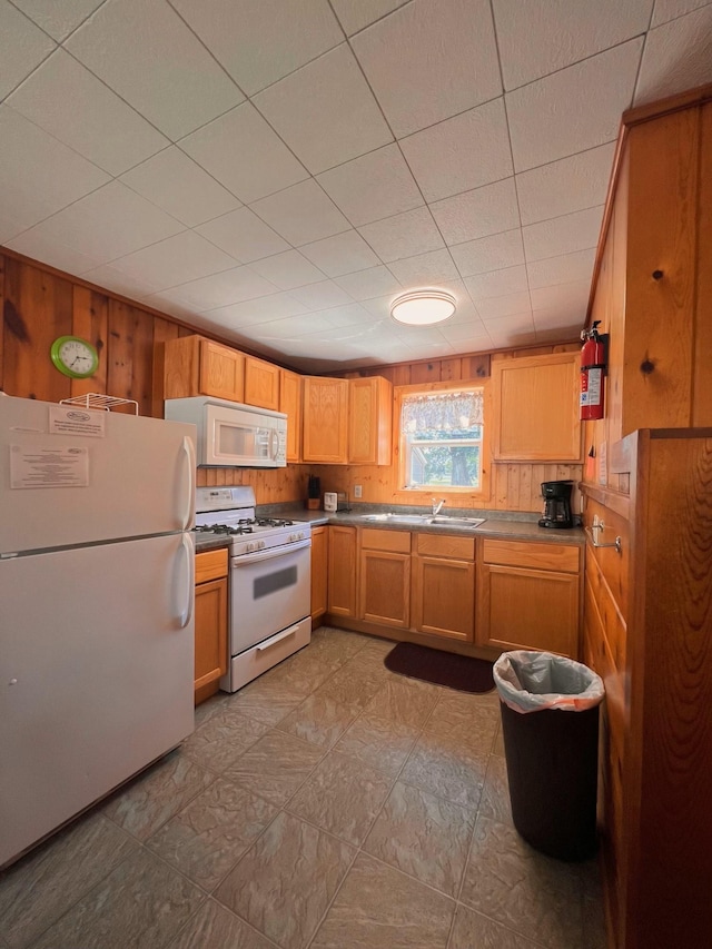 kitchen with white appliances, wood walls, and a sink