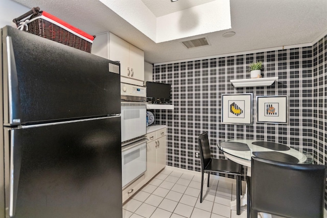 kitchen with visible vents, double oven, freestanding refrigerator, light tile patterned flooring, and white cabinetry