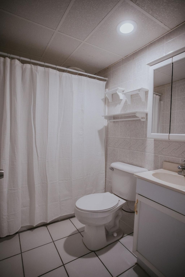 full bath featuring tile patterned flooring, tile walls, toilet, vanity, and a paneled ceiling